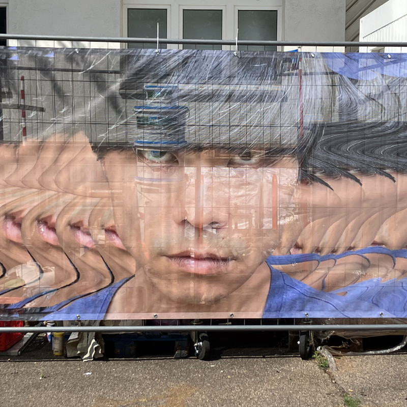big face printed on a banner hanging on a construction fence